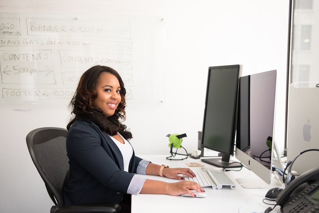 Confident businesswoman seated at her desk in an office, typing on a computer.